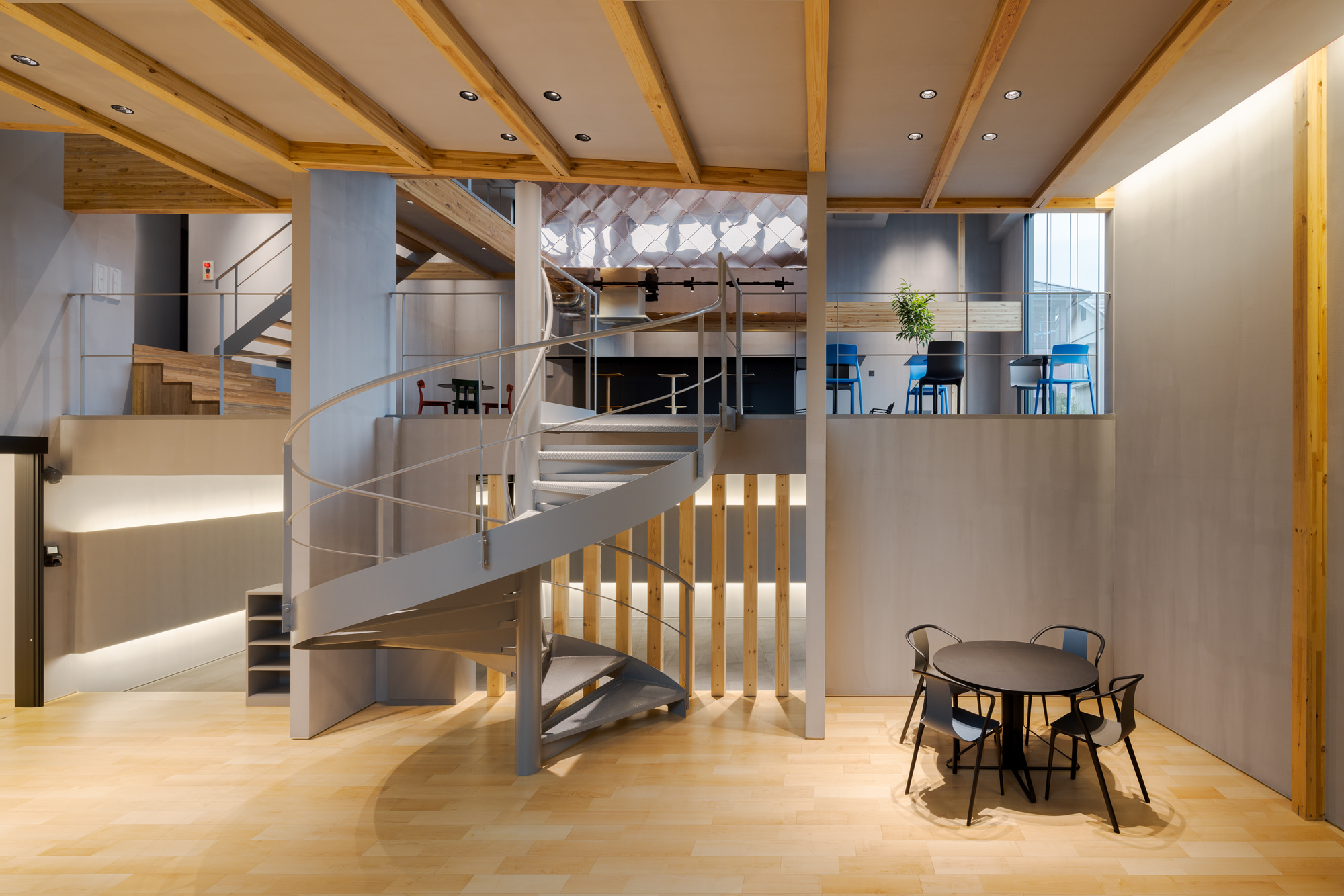 上の写真は、木造2階建て事務所ビルの事例です。  大開口に面して明るい大空間があり、様々なボリュームが重層する空間構成になっています。  ＜画像＞  スキップフロアの構成となっており、いろいろな広さや高さを体感できる建築です。  印象的な螺旋階段が空間をつなぎます。  関連記事：アクシスホールディングス新社屋