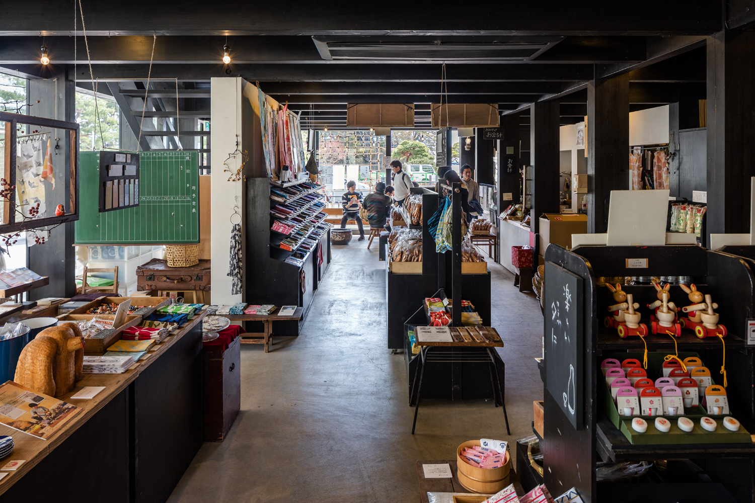 土産物屋、菓子店とその工場、カフェ、住宅からなる3階建ての複合建築の事例です。 東、南面に設けられた大きな庇の深い軒と軒裏の垂木が印象的な外観で、木造建築でありながら大きな開口部が特徴的です。 建物は東側に開いており、西側は隣接建物の壁を隠すように白い漆喰塗りの壁を立てて背景をつくり、その手前に開放的なスケルトンを置く、という構成となっています。 ＜画像＞ 普遍的で飽きのこないデザインとなっており、開放的な木造軸組架構により、モダンなテイストを実現しています。 1階は土産物屋として観光客が入りやすい開放的な店構えを実現しています。 2階は松島の美しい景観を望むカフェとして快適な眺望の確保を実現しています。 関連記事：SE構法の店舗の事例紹介「松華堂菓子店」